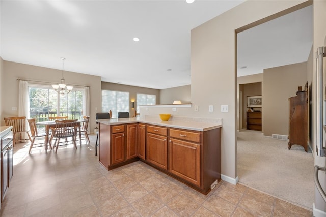 kitchen with brown cabinetry, light countertops, a chandelier, a peninsula, and hanging light fixtures