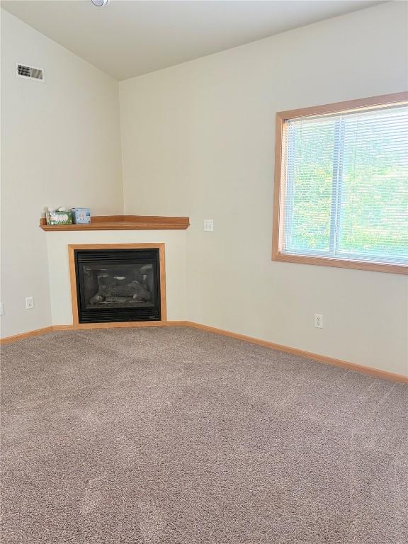 unfurnished living room with carpet flooring, a glass covered fireplace, and baseboards