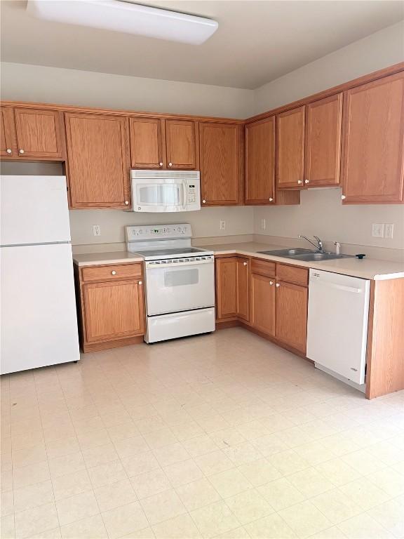 kitchen featuring white appliances, a sink, light countertops, and brown cabinets