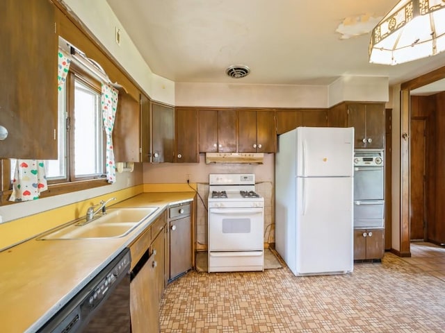 kitchen featuring white appliances, a sink, light countertops, a warming drawer, and brown cabinetry