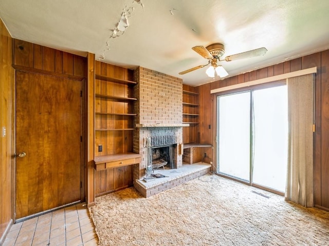 unfurnished living room with wooden walls, a fireplace, a ceiling fan, built in shelves, and light tile patterned floors