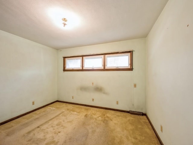 spare room featuring light colored carpet and baseboards