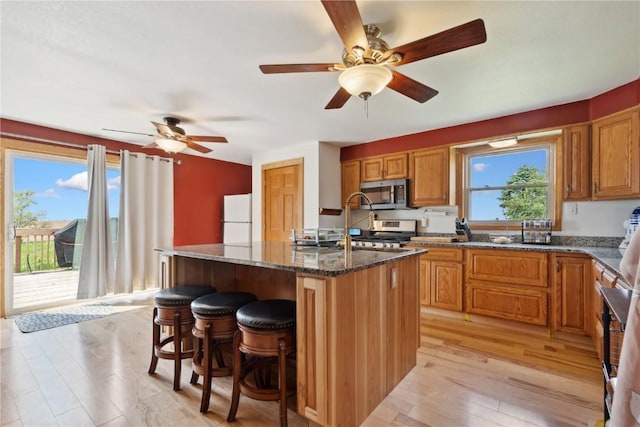 829 Union Ave, Lowden, IA 52255 - kitchen featuring stainless steel microwave, freestanding refrigerator, a kitchen island with sink, dark stone counters, and a kitchen breakfast bar
