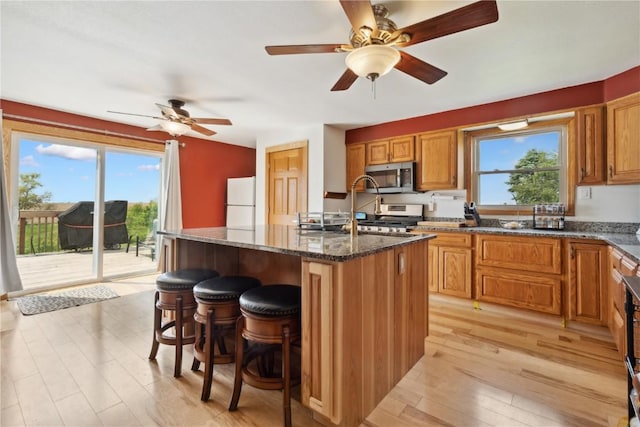 829 Union Ave, Lowden, IA 52255 - kitchen with stainless steel appliances, light wood finished floors, dark stone counters, a breakfast bar area, and an island with sink
