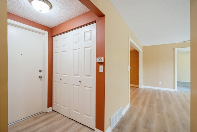 entrance foyer with light wood-style flooring, a textured ceiling, and baseboards