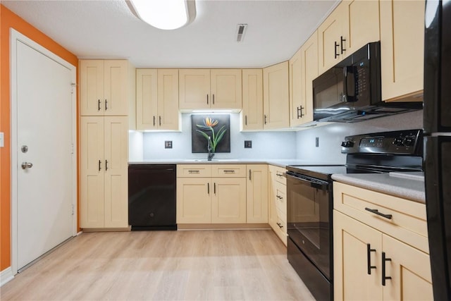 kitchen with black appliances, light wood-style floors, light countertops, and cream cabinetry