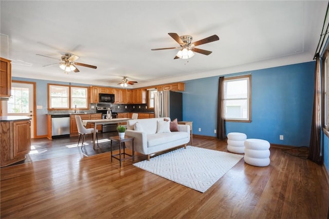 living room with dark wood-type flooring, ceiling fan, and baseboards