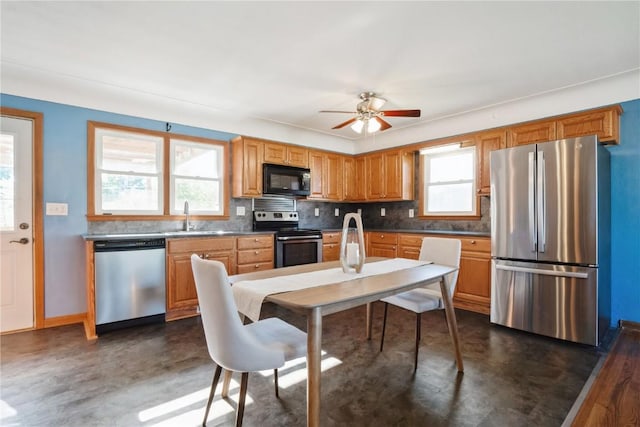 kitchen with appliances with stainless steel finishes, a sink, decorative backsplash, ceiling fan, and concrete flooring