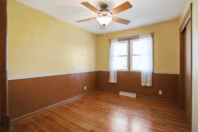 spare room with wood finished floors, baseboards, a ceiling fan, and a textured wall