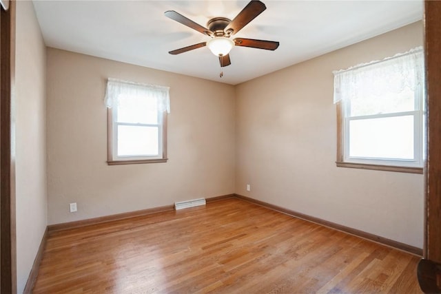 spare room featuring healthy amount of natural light, light wood-type flooring, a ceiling fan, and baseboards