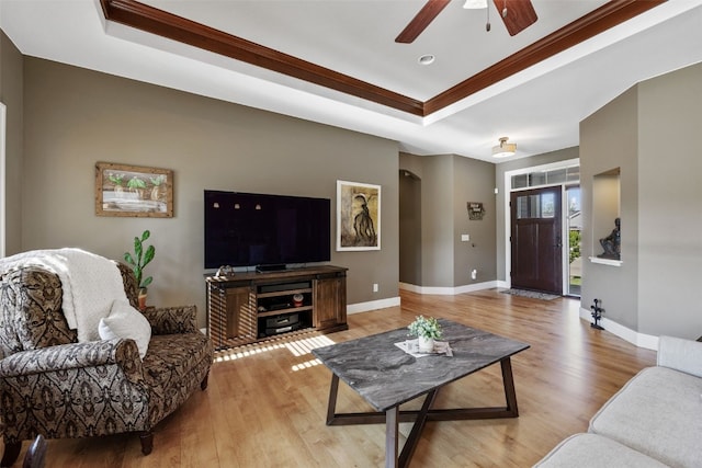living area with a tray ceiling, a ceiling fan, light wood-style flooring, and ornamental molding