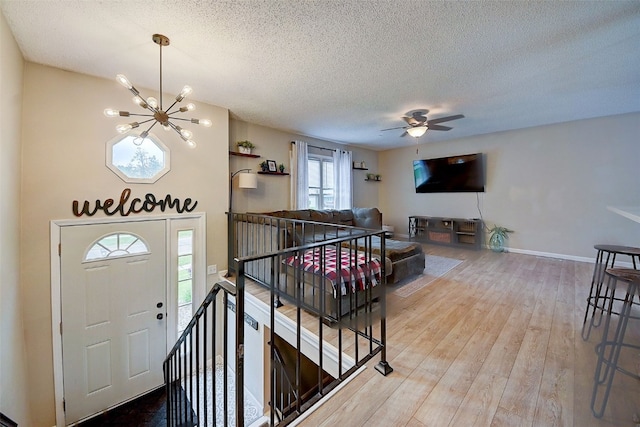 entrance foyer featuring a chandelier, a textured ceiling, wood finished floors, baseboards, and ceiling fan