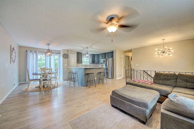 living area featuring a chandelier, a textured ceiling, light wood-style flooring, ceiling fan, and baseboards