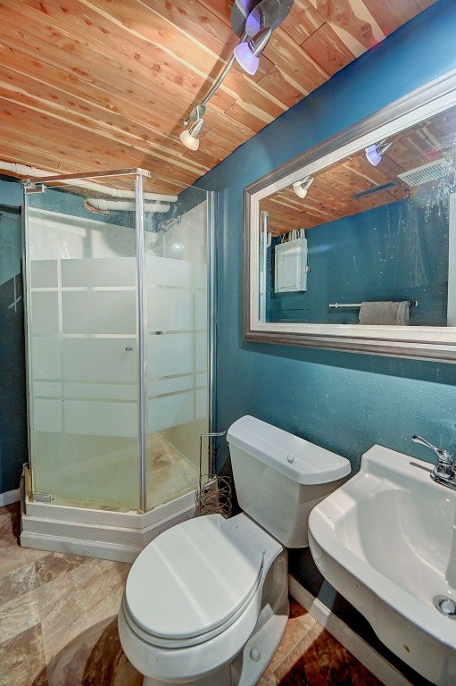 bathroom featuring wood ceiling, toilet, a stall shower, and a sink