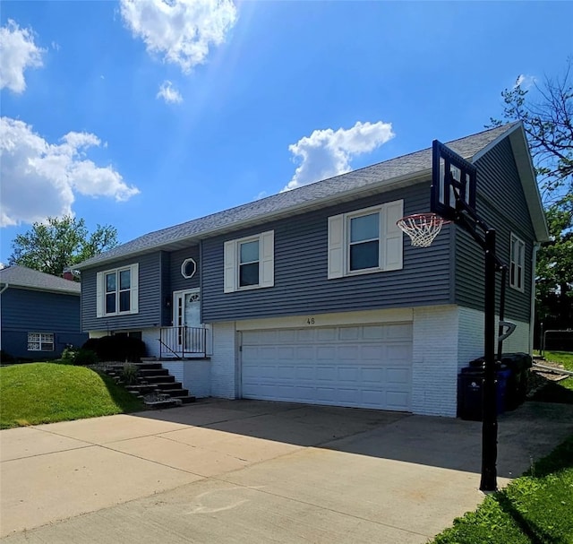 bi-level home featuring brick siding, a garage, concrete driveway, and a front yard