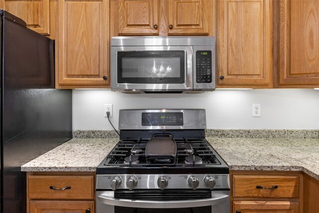 1451 Chamberlain Dr, Iowa City, IA 52240 - kitchen featuring appliances with stainless steel finishes, light stone counters, and brown cabinetry