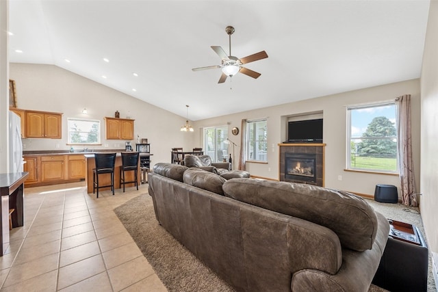 living room with light tile patterned floors, a ceiling fan, a fireplace, a chandelier, and high vaulted ceiling