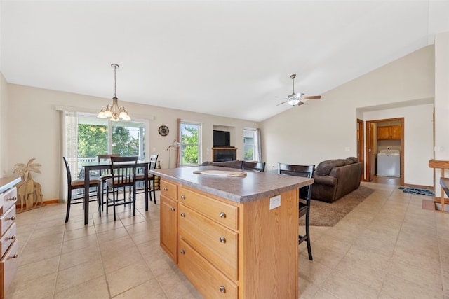 kitchen with washer / clothes dryer, vaulted ceiling, a chandelier, a ceiling fan, and a center island
