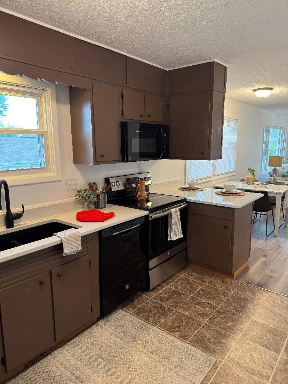 3105 Wilson Ave SW, Cedar Rapids, IA 52404 - kitchen with black appliances, a sink, a textured ceiling, light countertops, and a peninsula