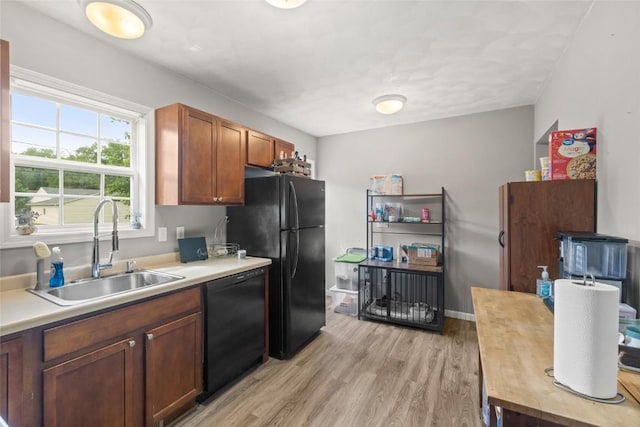 kitchen featuring black appliances, a sink, light wood finished floors, light countertops, and brown cabinets