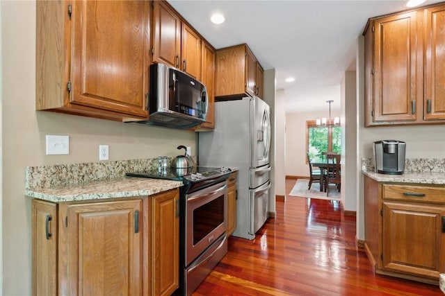 1445 NE Butternut Ln, Swisher, IA 52338 - kitchen featuring stainless steel appliances, dark wood finished floors, brown cabinetry, a chandelier, and light stone countertops