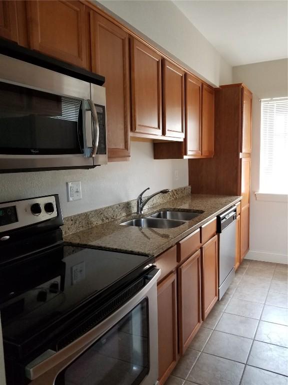 100 Granview Ct Unit 126, Iowa City, IA 52246 - kitchen featuring stainless steel appliances, a sink, brown cabinets, stone counters, and light tile patterned floors