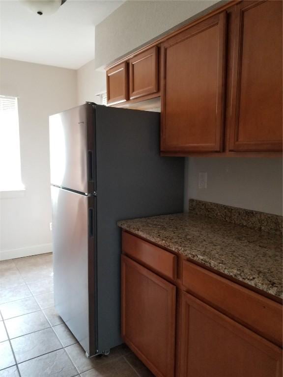 100 Granview Ct Unit 126, Iowa City, IA 52246 - kitchen featuring freestanding refrigerator, brown cabinetry, light tile patterned floors, and light stone counters