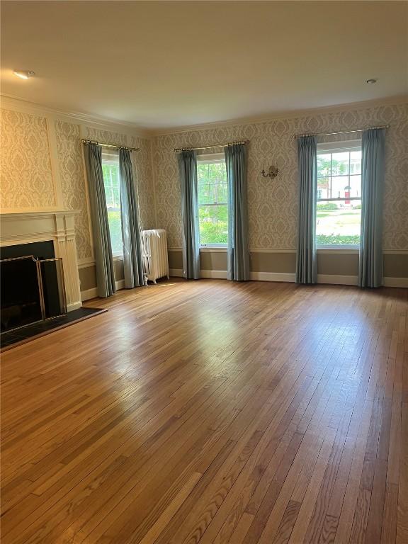 620 S Summit St, Iowa City, IA 52240 - unfurnished living room featuring radiator, wallpapered walls, healthy amount of natural light, hardwood / wood-style floors, and ornamental molding