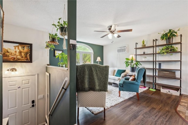 607 E Pershing Dr, Brooklyn, IA 52211 - living area with ceiling fan, wood finished floors, a wall unit AC, baseboards, and a textured ceiling