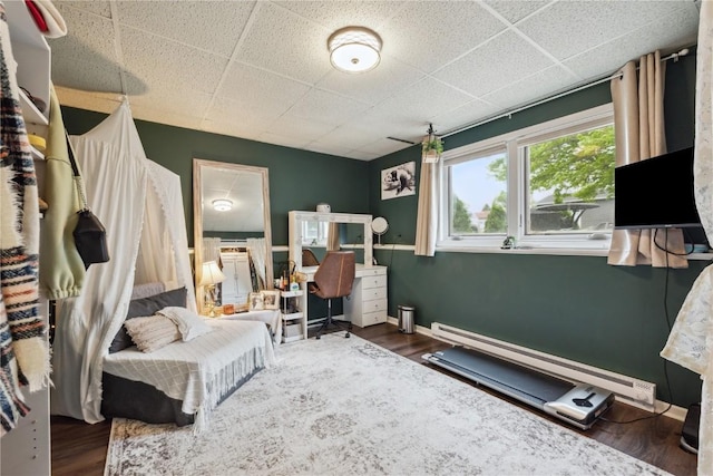 607 E Pershing Dr, Brooklyn, IA 52211 - bedroom with baseboard heating, wood finished floors, and a paneled ceiling