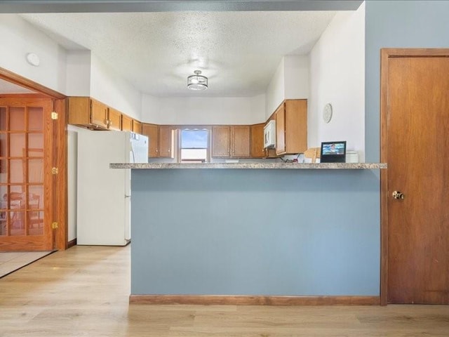 433 S Iowa St, Solon, IA 52333 - kitchen featuring white appliances, brown cabinets, a peninsula, light wood-style floors, and a textured ceiling