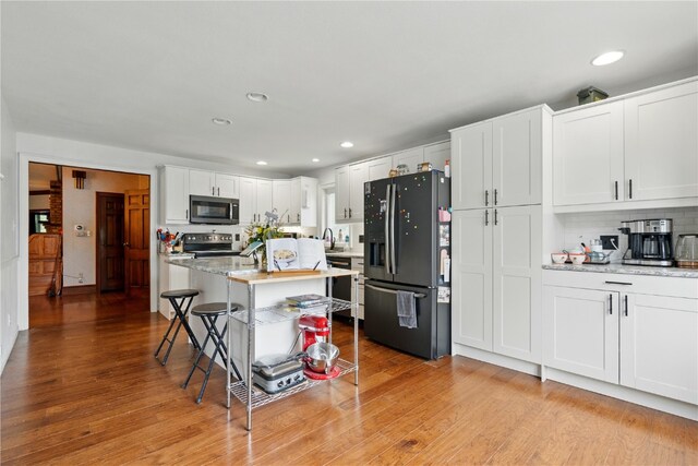 205 S Ford St, Anamosa, IA 52205 - kitchen featuring black appliances, a kitchen breakfast bar, light wood-style flooring, white cabinetry, and recessed lighting