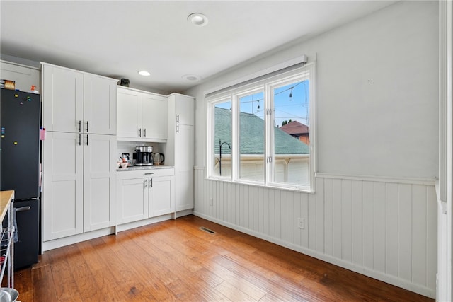 205 S Ford St, Anamosa, IA 52205 - kitchen with light wood-style flooring, wainscoting, freestanding refrigerator, white cabinetry, and light countertops