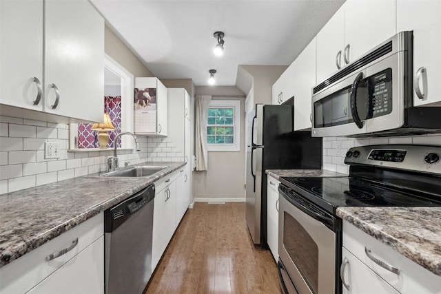 3051 Wayne Ave Unit 64, Iowa City, IA 52240 - kitchen with stainless steel appliances, a sink, white cabinets, light wood-type flooring, and backsplash
