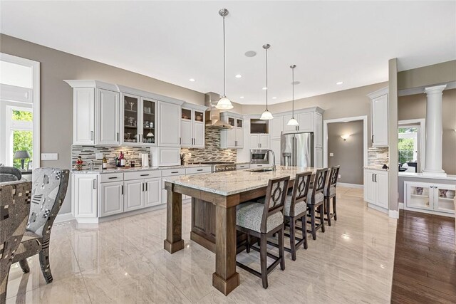6712 Spring Grove Ct NE, Cedar Rapids, IA 52411 - kitchen with stainless steel fridge with ice dispenser, wall chimney range hood, tasteful backsplash, ornate columns, and a kitchen bar