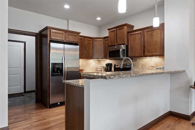 2913 Caspian Rd, Hiawatha, IA 52233 - kitchen with appliances with stainless steel finishes, light wood-style floors, a peninsula, decorative backsplash, and light stone counters
