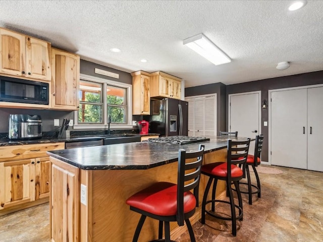 1901 42nd St SE, Cedar Rapids, IA 52403 - kitchen with black appliances, light brown cabinetry, dark countertops, a textured ceiling, and a kitchen bar