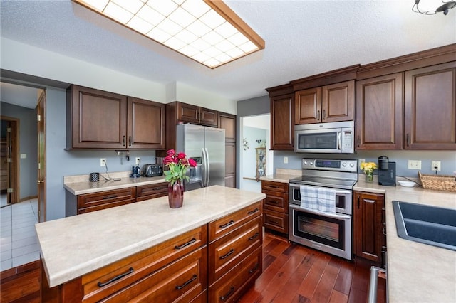 6919 Rockingham Dr SW, Cedar Rapids, IA 52404 - kitchen with appliances with stainless steel finishes, light countertops, dark wood finished floors, a kitchen island, and dark brown cabinetry
