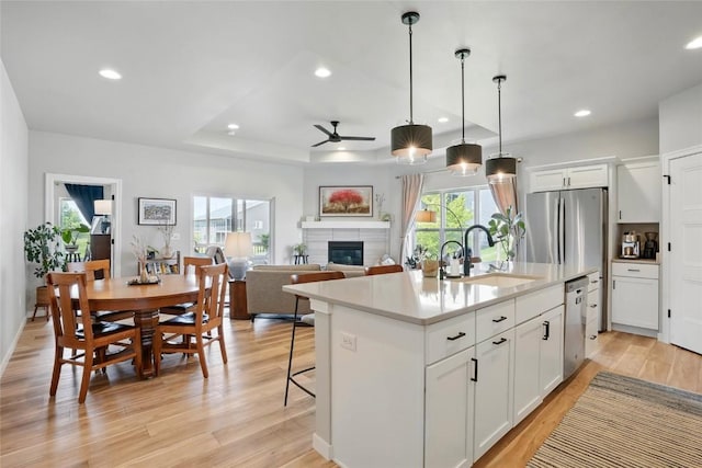 927 Summit Ct, Tiffin, IA 52340 - kitchen featuring a sink, ceiling fan, appliances with stainless steel finishes, light wood-style flooring, and a glass covered fireplace
