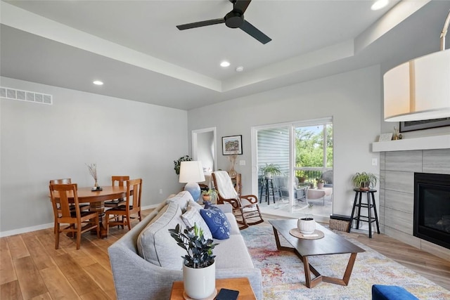 927 Summit Ct, Tiffin, IA 52340 - living room with a tray ceiling, a ceiling fan, a tiled fireplace, light wood-style flooring, and recessed lighting