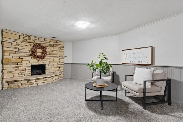 1004 W Welsh St, Williamsburg, IA 52361 - living room with a textured ceiling, carpet flooring, a wainscoted wall, a stone fireplace, and crown molding