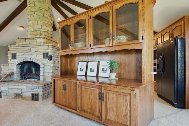 1004 W Welsh St, Williamsburg, IA 52361 - kitchen featuring black fridge, light carpet, glass insert cabinets, brown cabinetry, and a stone fireplace