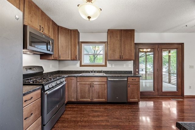 2536 N Ave NW, Cedar Rapids, IA 52405 - kitchen with appliances with stainless steel finishes, dark countertops, a textured ceiling, dark wood finished floors, and a sink