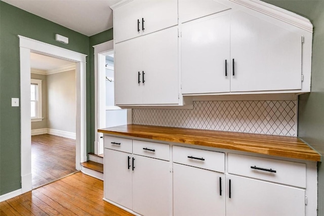 384 21st St SE, Cedar Rapids, IA 52403 - kitchen with light wood finished floors, backsplash, wooden counters, white cabinetry, and crown molding