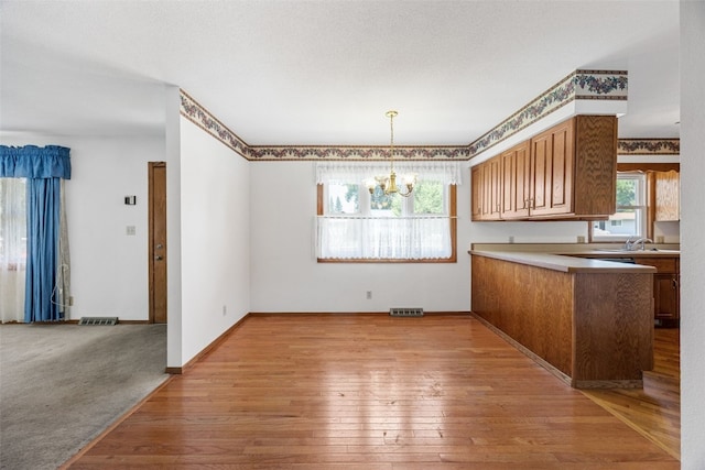 1083 Rainbow Blvd, Hiawatha, IA 52233 - kitchen featuring a chandelier, light wood-type flooring, brown cabinetry, a sink, and light countertops