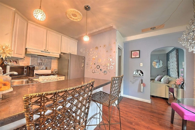 361 30th St SE, Cedar Rapids, IA 52403 - kitchen featuring under cabinet range hood, arched walkways, freestanding refrigerator, dark wood-style floors, and decorative light fixtures