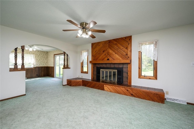 409 Oak St, Rowley, IA 52329 - unfurnished living room with a ceiling fan, carpet floors, a tiled fireplace, arched walkways, and wooden walls
