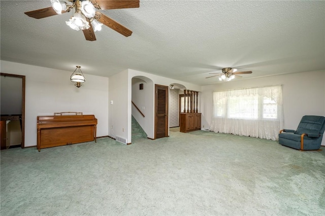 409 Oak St, Rowley, IA 52329 - unfurnished living room featuring ceiling fan, light colored carpet, stairway, a textured ceiling, and arched walkways