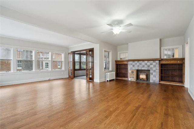 2325 Grande Ave SE, Cedar Rapids, IA 52403 - unfurnished living room with radiator heating unit, ceiling fan, wood finished floors, baseboards, and a tiled fireplace