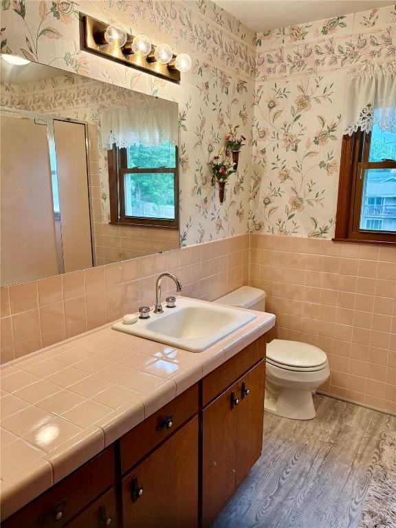 832 17th St SE, Cedar Rapids, IA 52403 - bathroom featuring wallpapered walls, wood finished floors, vanity, a wainscoted wall, and tile walls